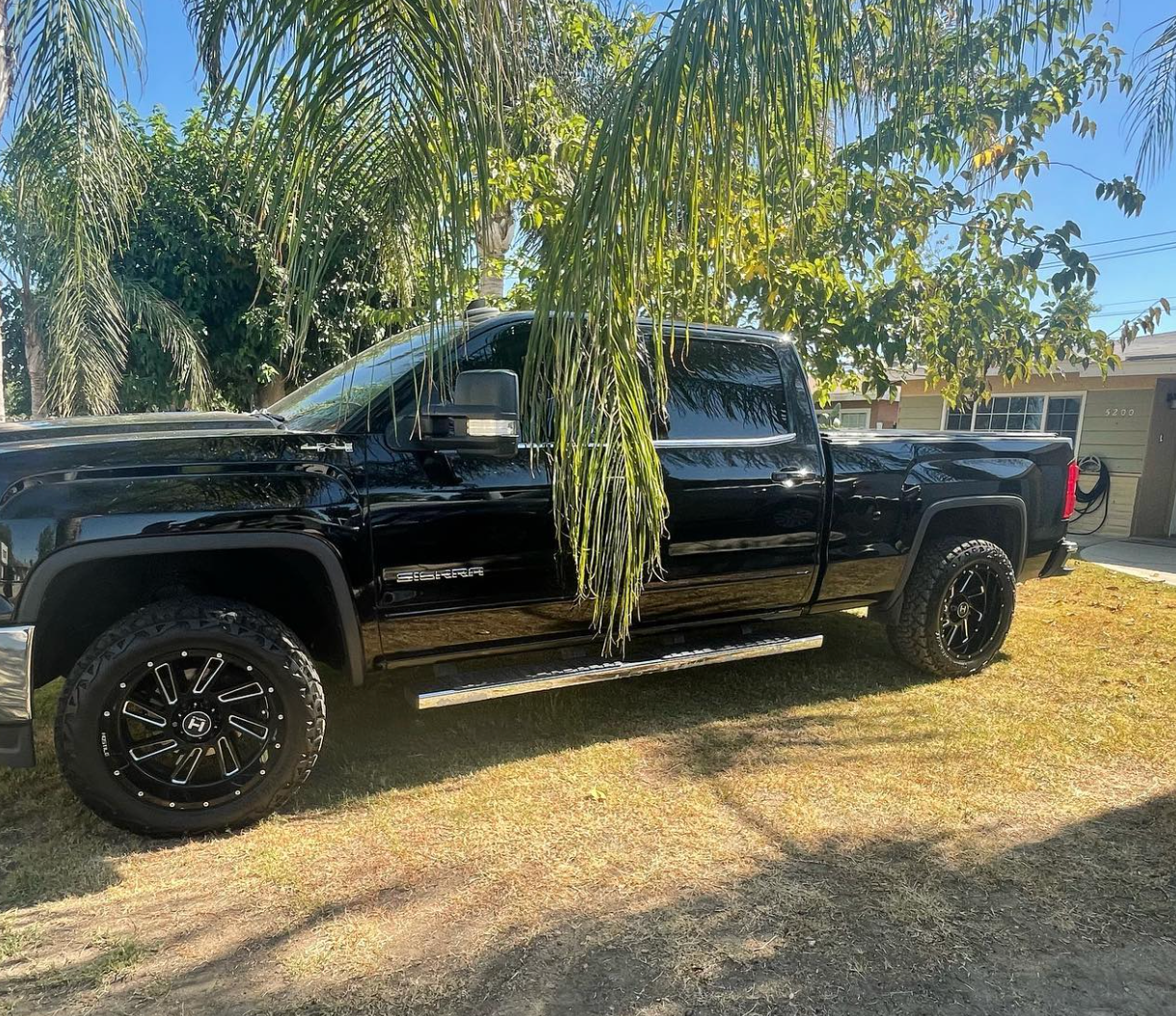 A black truck is parked in the grass in front of a house.