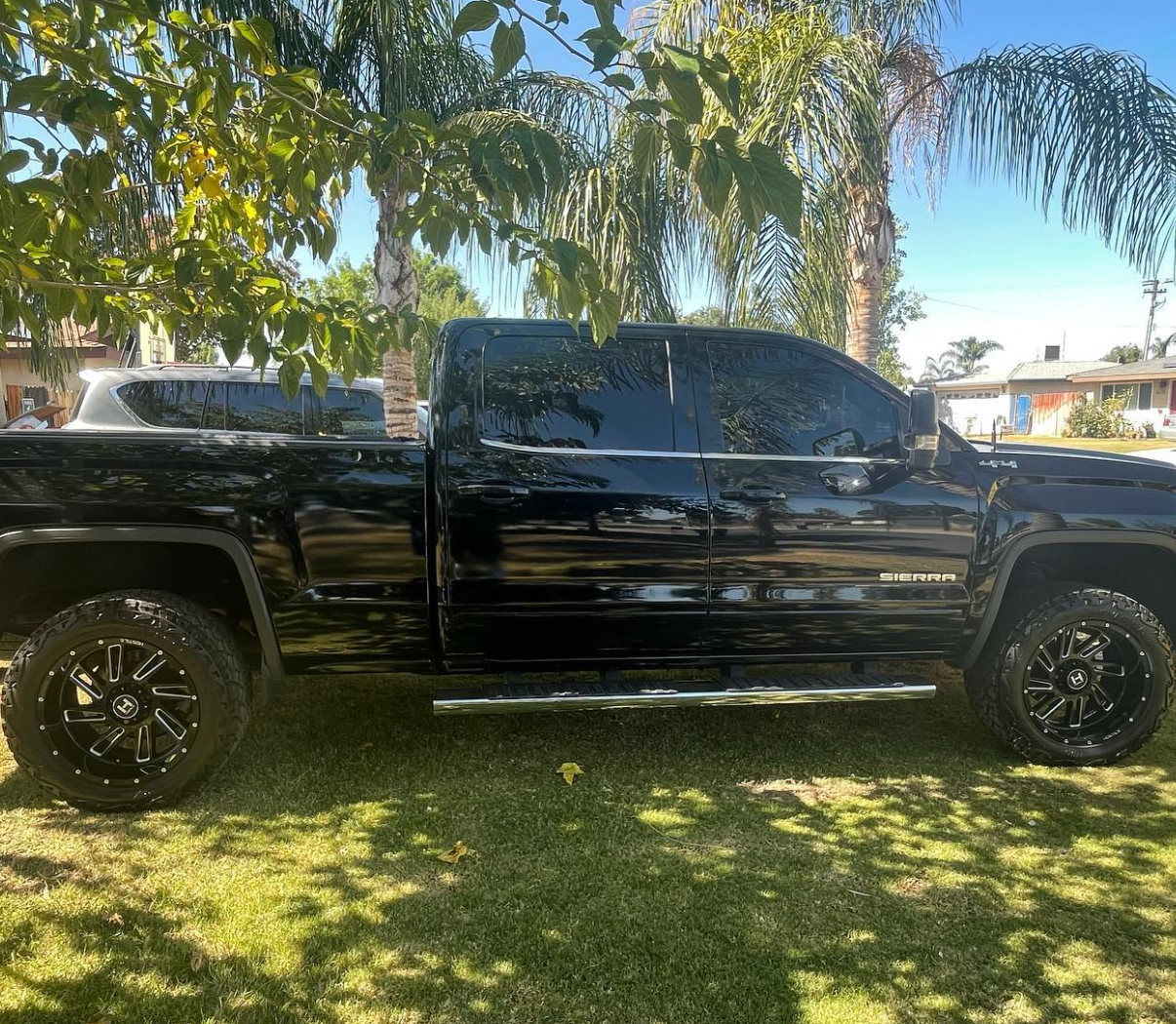 A black truck is parked in the grass under a tree.