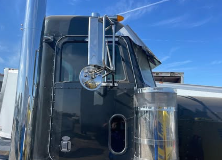 A black semi truck with a chrome exhaust pipe is parked in a parking lot.