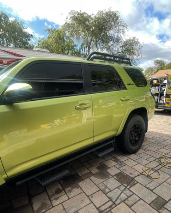 A green suv is parked on a brick driveway.