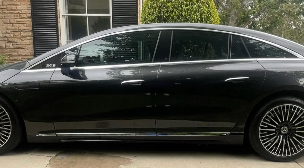 A black car is parked in a driveway in front of a house.