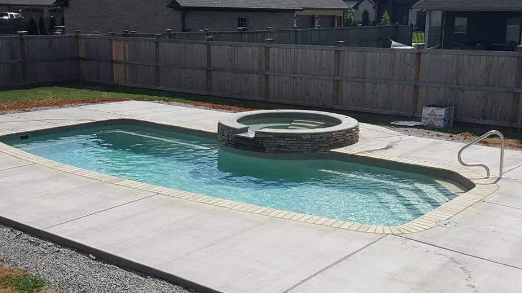 A swimming pool with a hot tub in the backyard of a house.