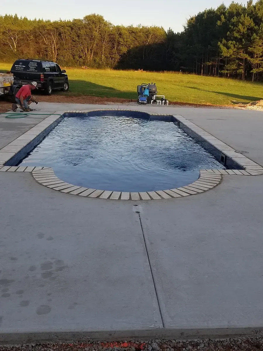 A man is standing next to a large swimming pool.