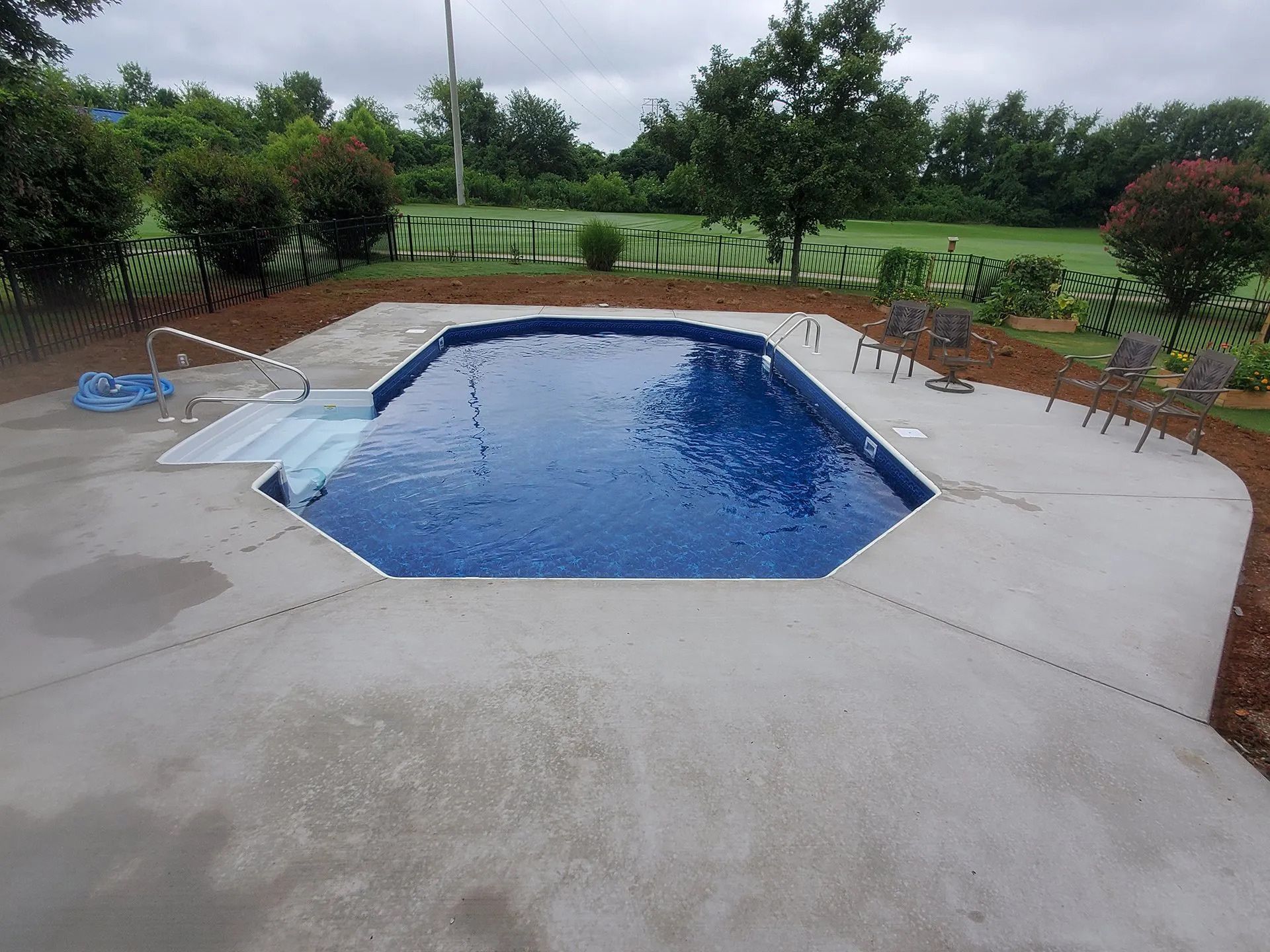 A large swimming pool is surrounded by chairs and trees