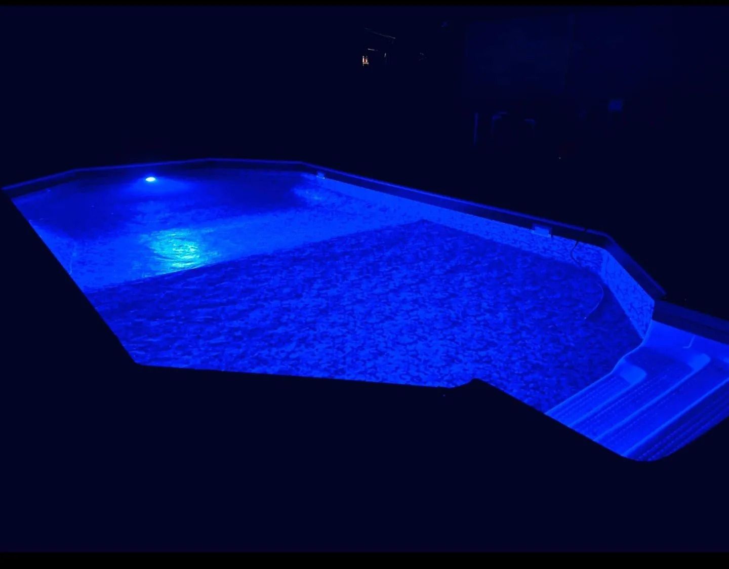 A swimming pool is lit up with blue lights at night.