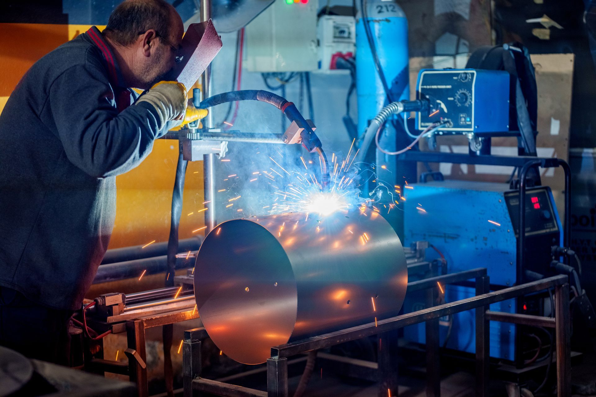 A man is welding a metal pipe in a factory.