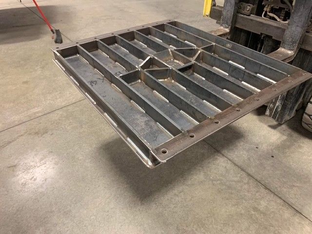 A metal pallet is sitting on a concrete floor next to a forklift.