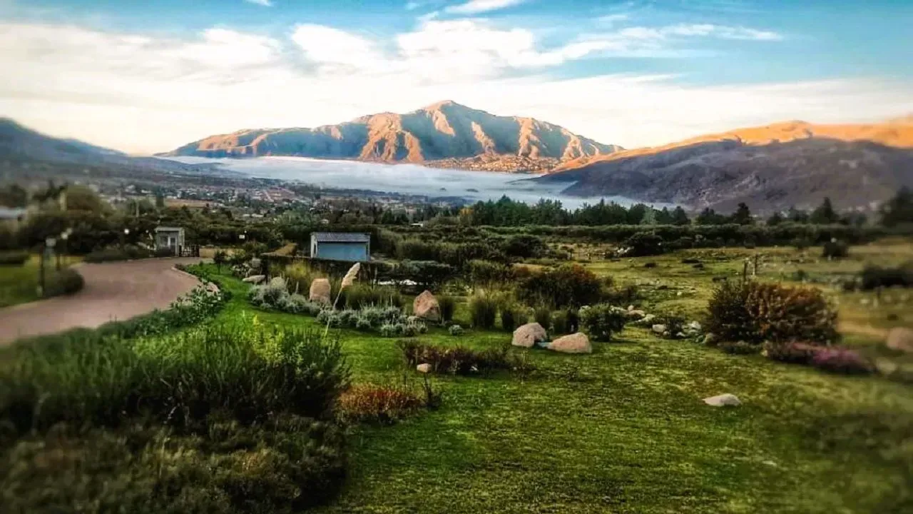 Exuberante paisaje verde con montañas y un valle envuelto en niebla bajo un cielo azul.