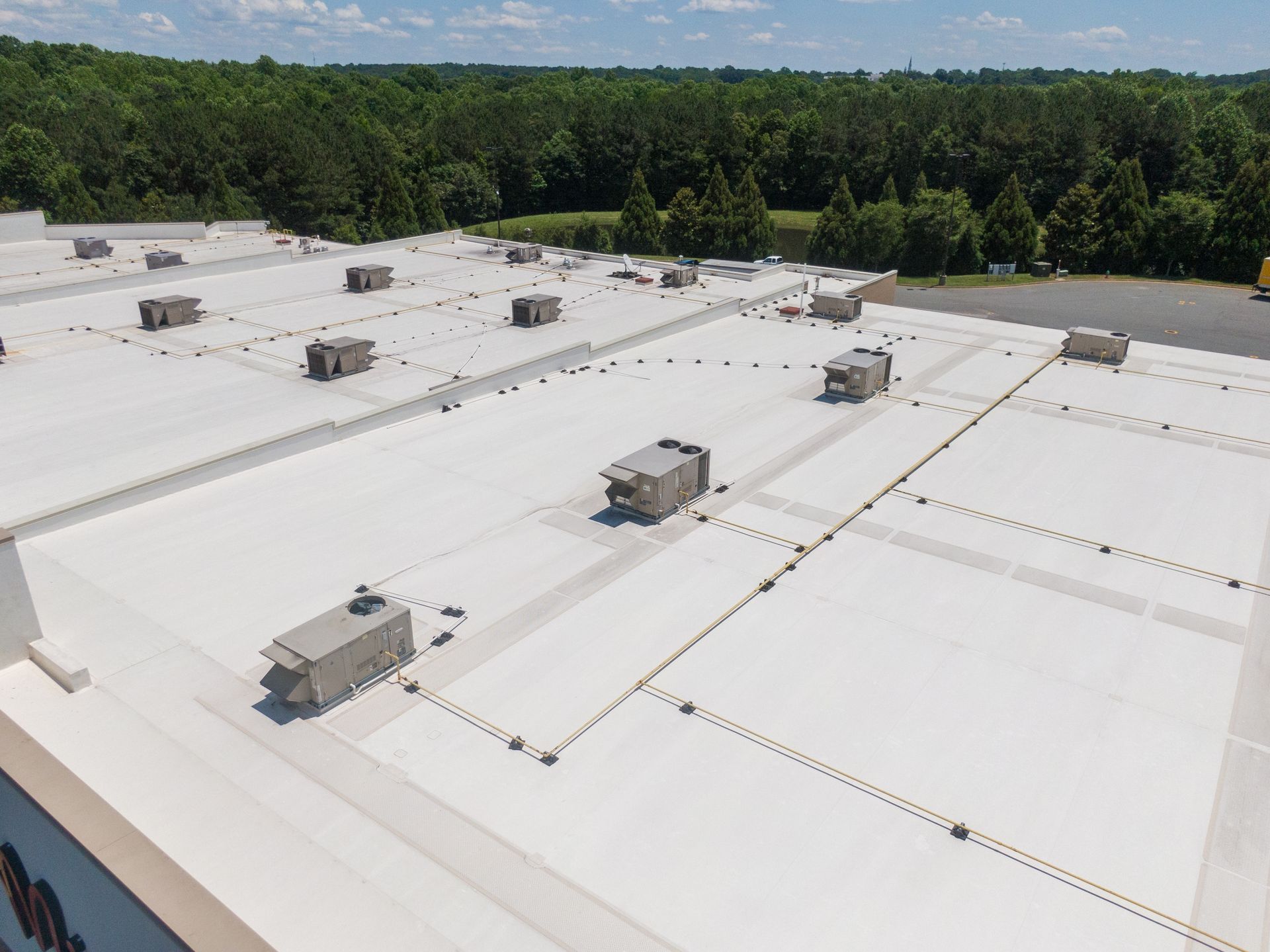 Aerial view of a white commercial roof with multiple HVAC units and connecting pathways against a backdrop of trees.