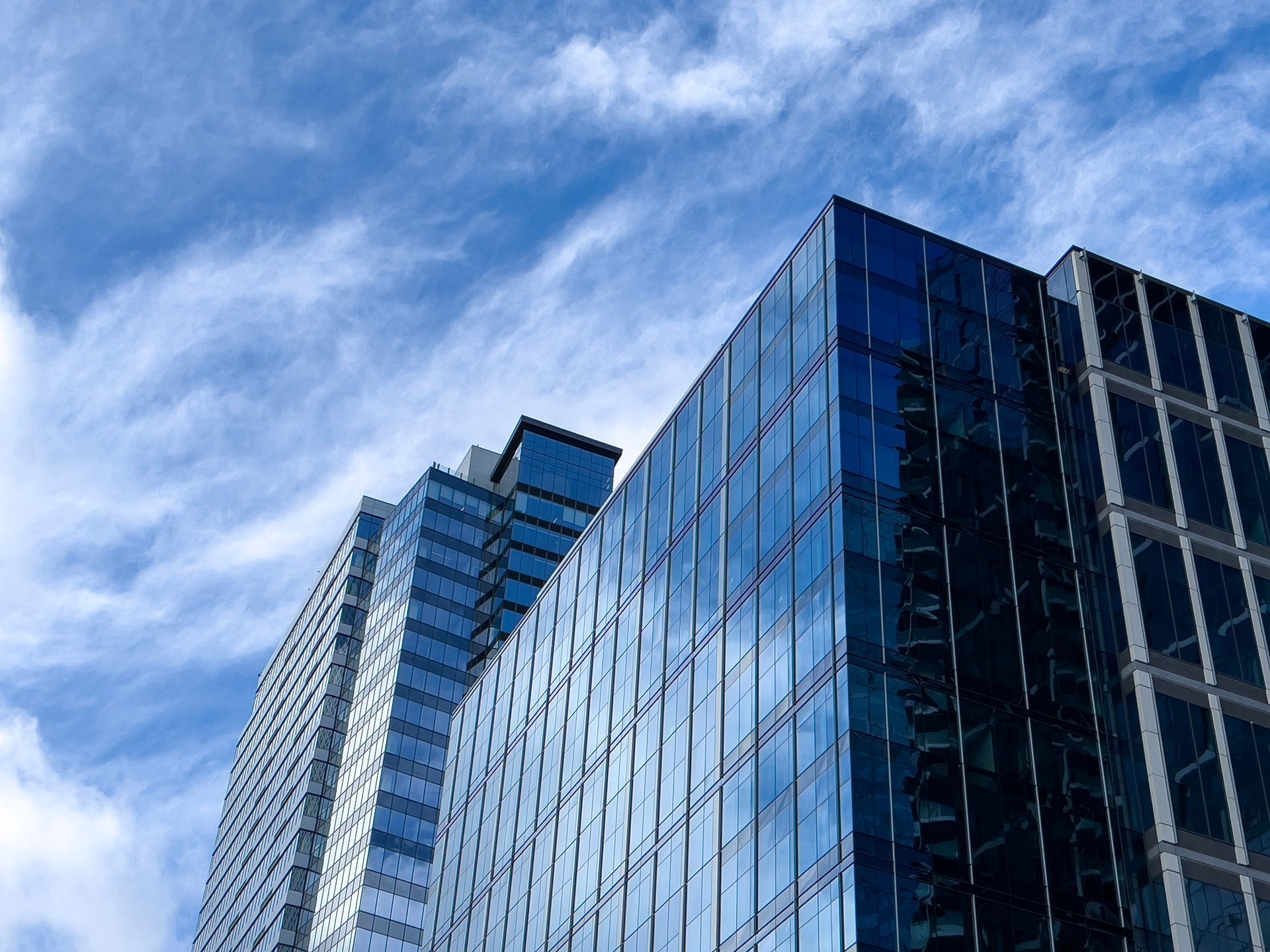 Modern glass-walled office buildings rise against a bright blue sky with wispy clouds.