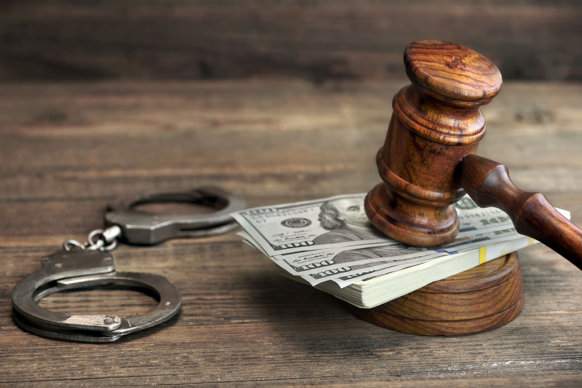 Handcuffs, money, and gavel on a wooden surface, symbolizing legal and financial concepts.