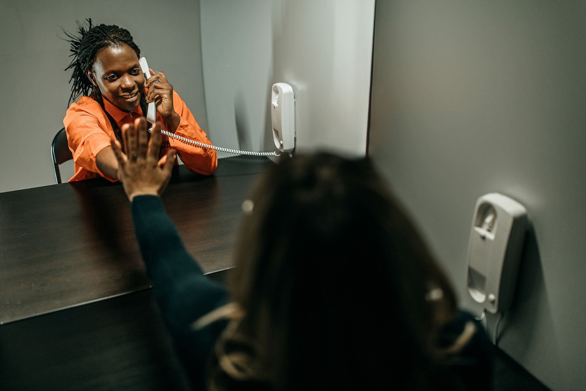 A prisoner behind a glass partition stretching out her hand towards her sister, who is visiting. A prisoner behind a glass partition stretching out her hand towards her sister, who is visiting.