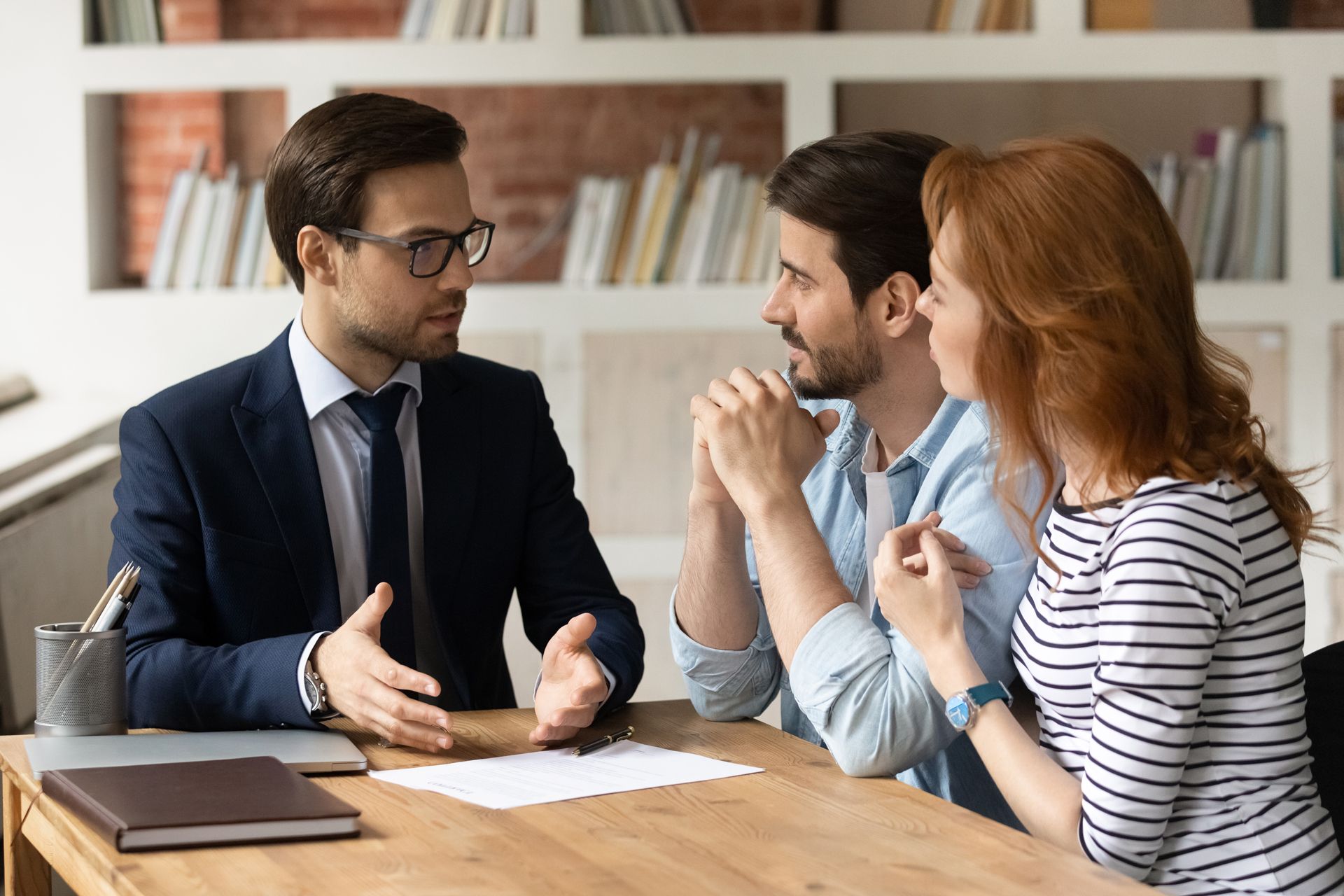 A man in a suit and tie is sitting at a table talking to a couple.