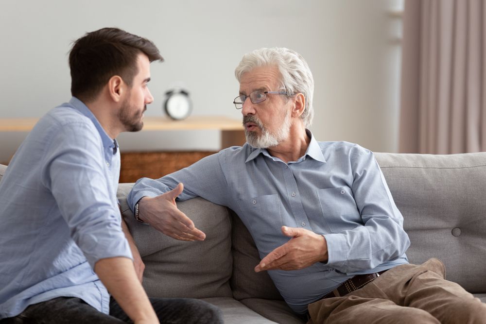 Two men are sitting on a couch talking to each other.