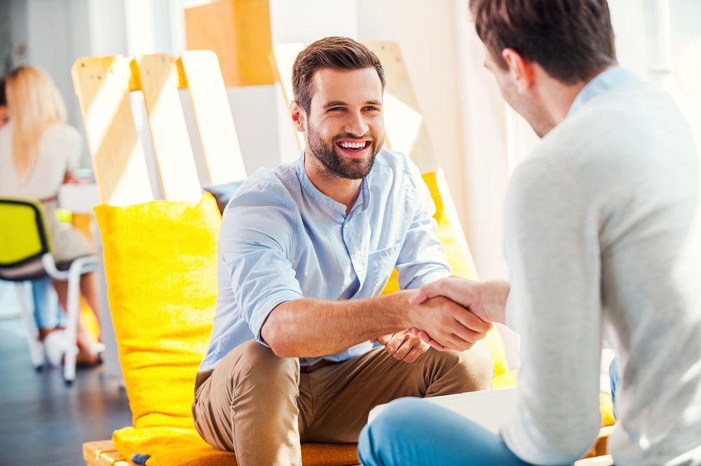 Two men are shaking hands while sitting on a yellow chair.