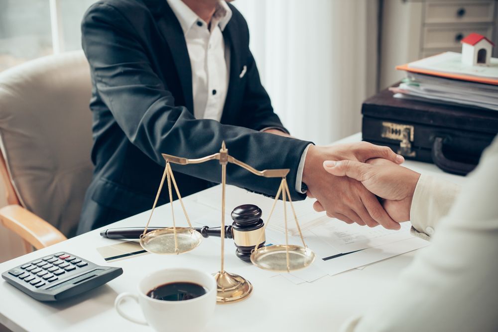 A man in a suit is shaking hands with a woman in front of a scale of justice.