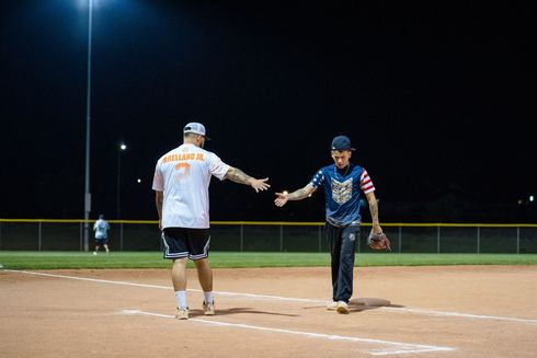 Two baseball players shake hands on the field under stadium lights at night.