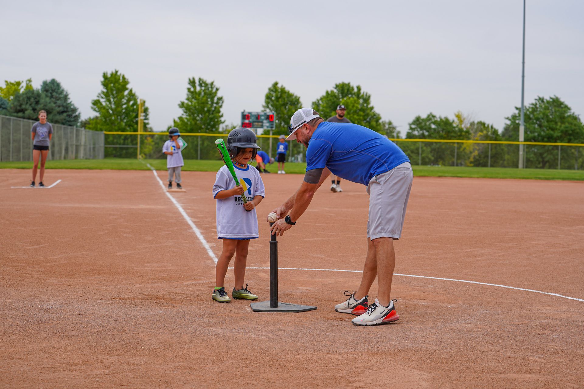 Coach adjusting a child’s batting tee on a softball field during practice