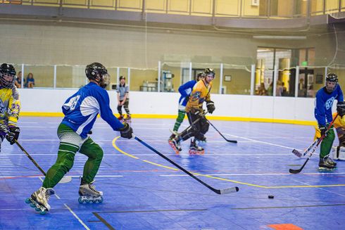 Inline hockey players in blue and yellow jerseys on a rink, skating after the puck