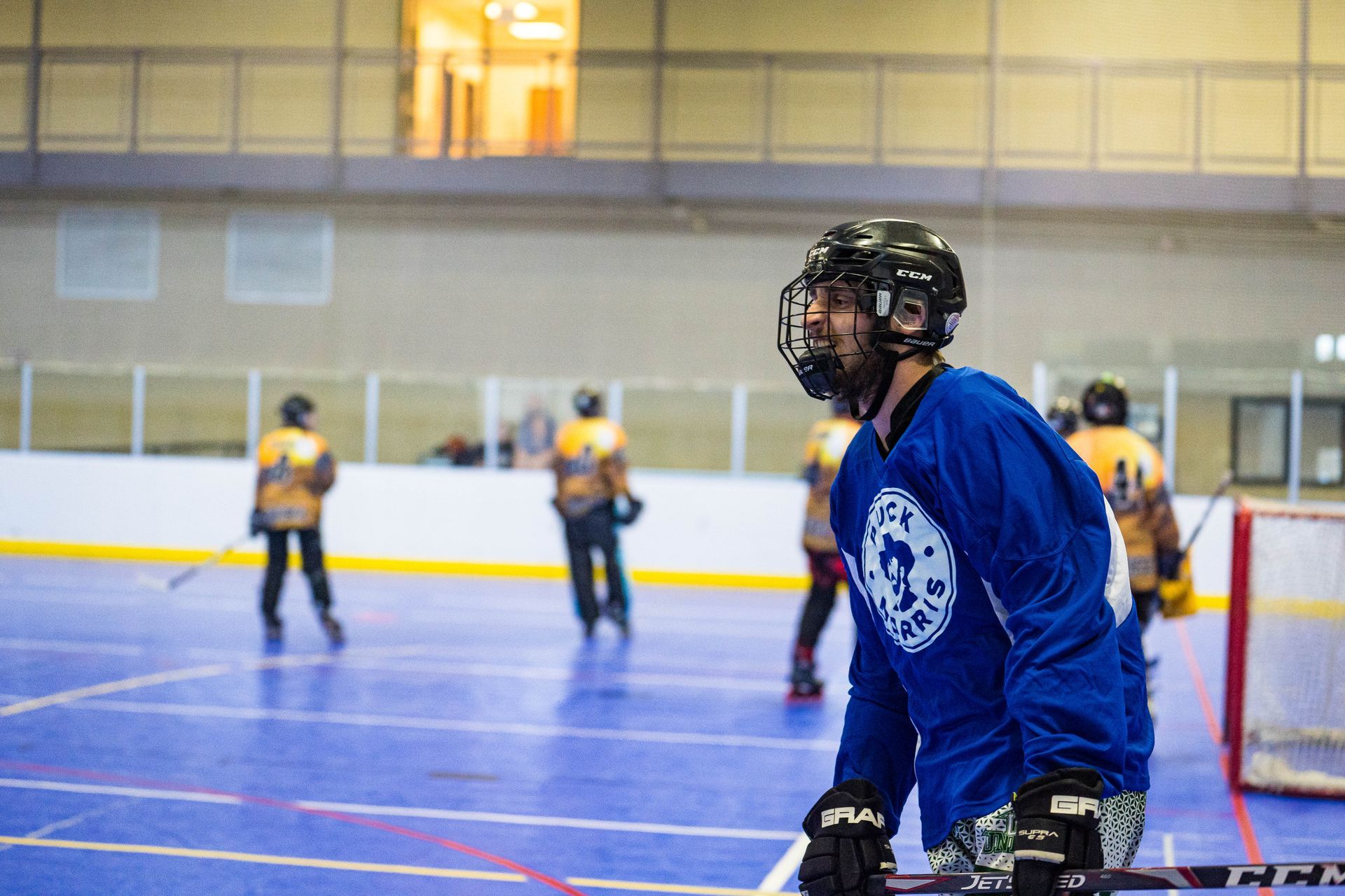 Inline hockey player in blue jersey on a rink, with blurred players and net in the background