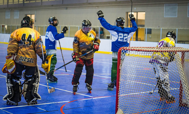 Indoor floor hockey game with players in colorful jerseys celebrating near the goal net