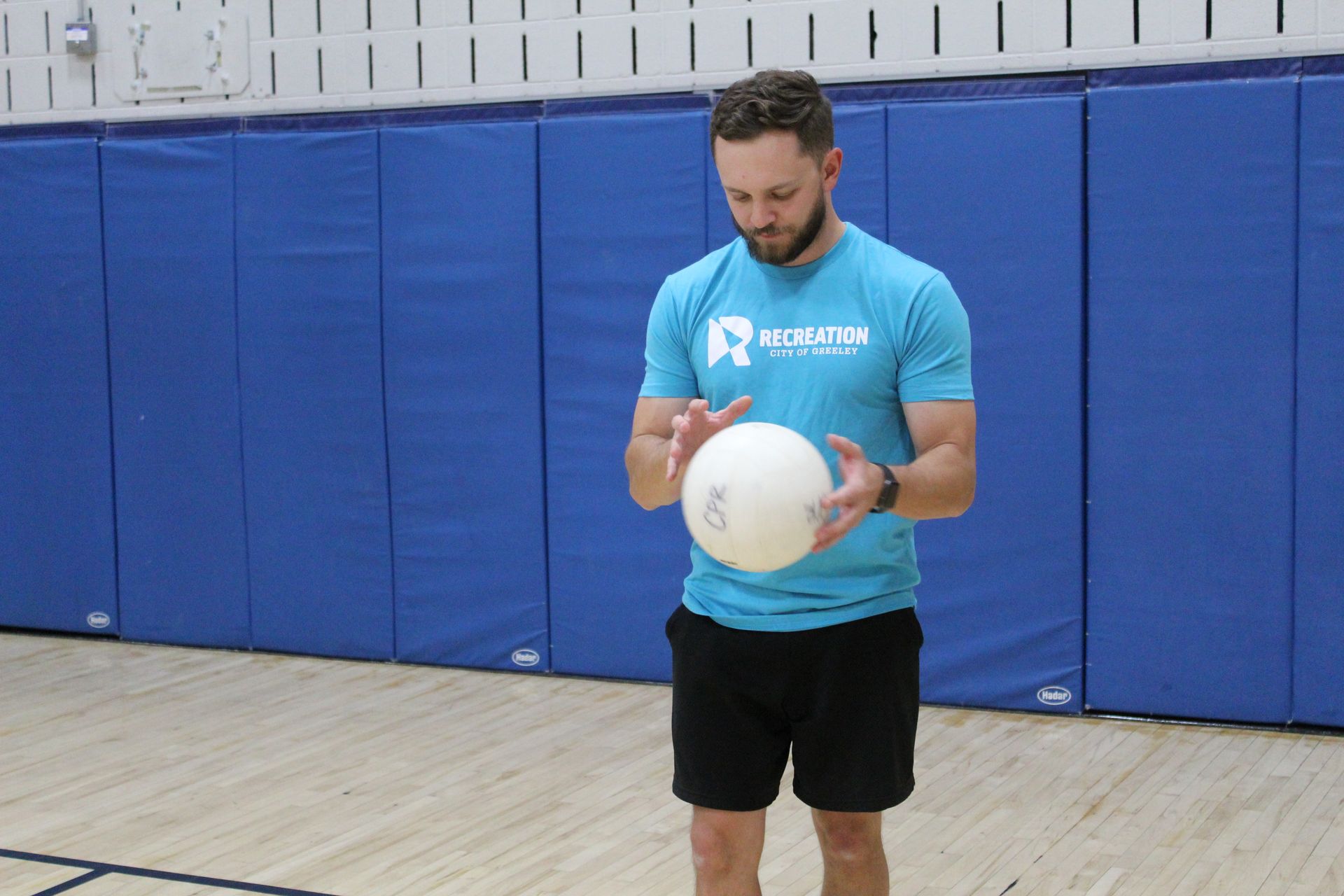 Man in blue shirt and black shorts holding a volleyball in a gymnasium