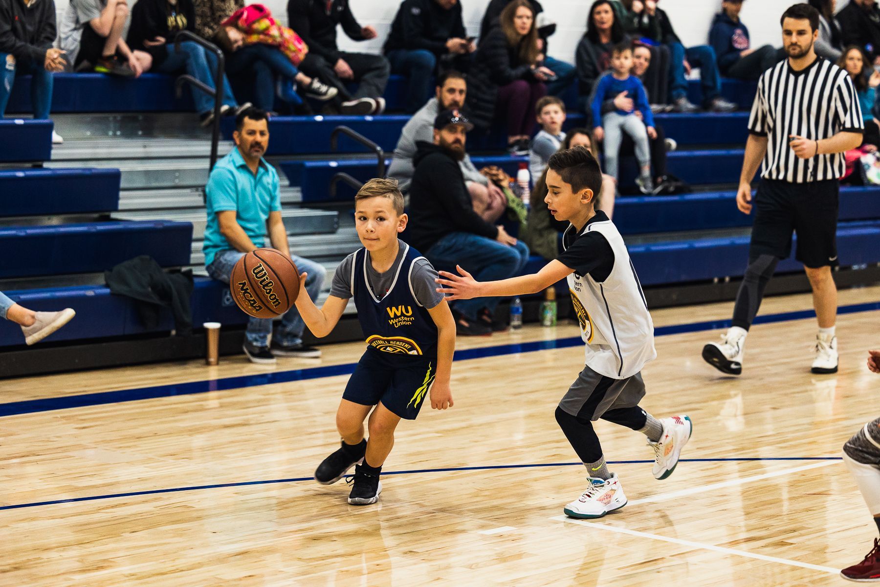 Youth basketball game with a child dribbling past a defender on a gym court