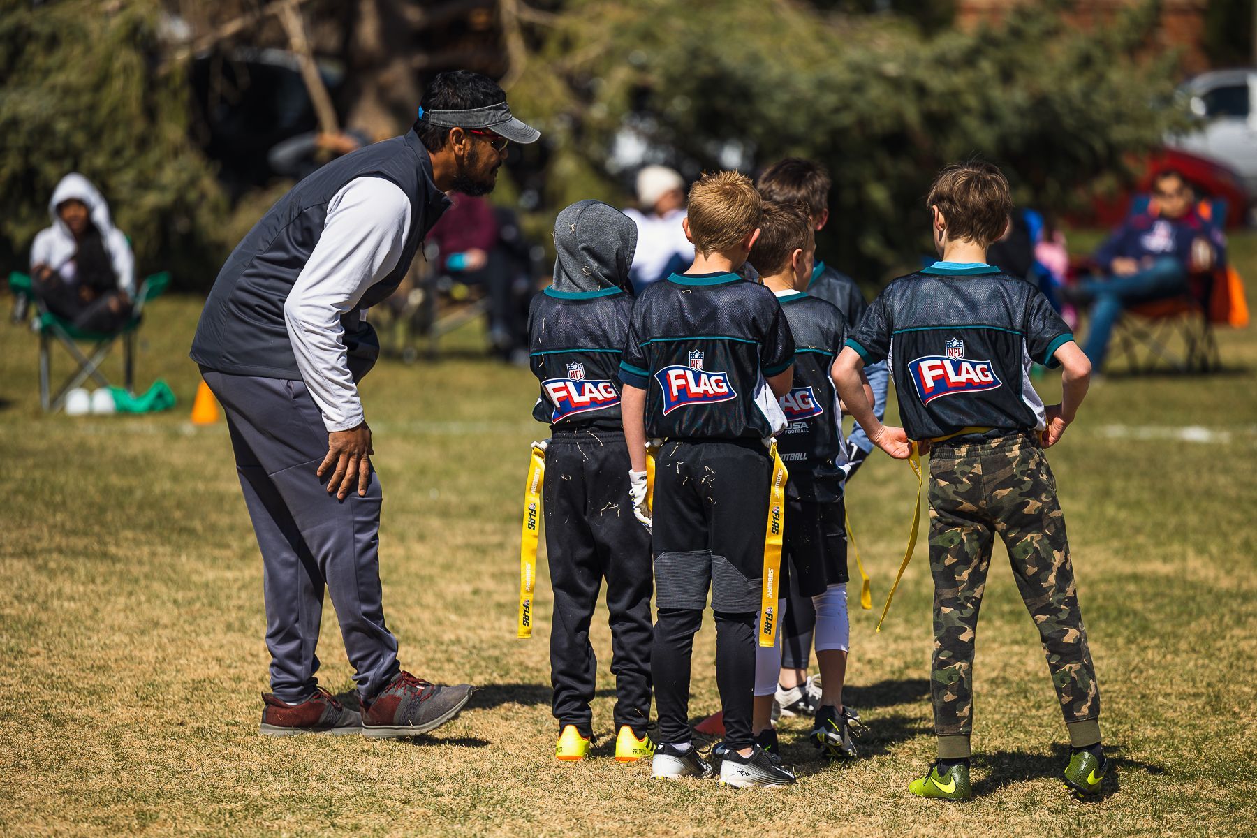 Coach talks to three youth players on a grassy field during a sports practice.