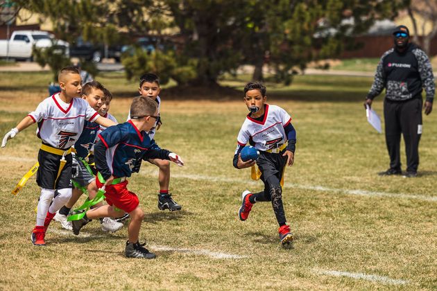 Children playing flag football on a grassy field, with a coach standing nearby.
