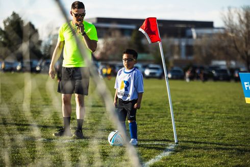 Soccer referee in neon shirt standing beside a child near the corner flag on a grassy field