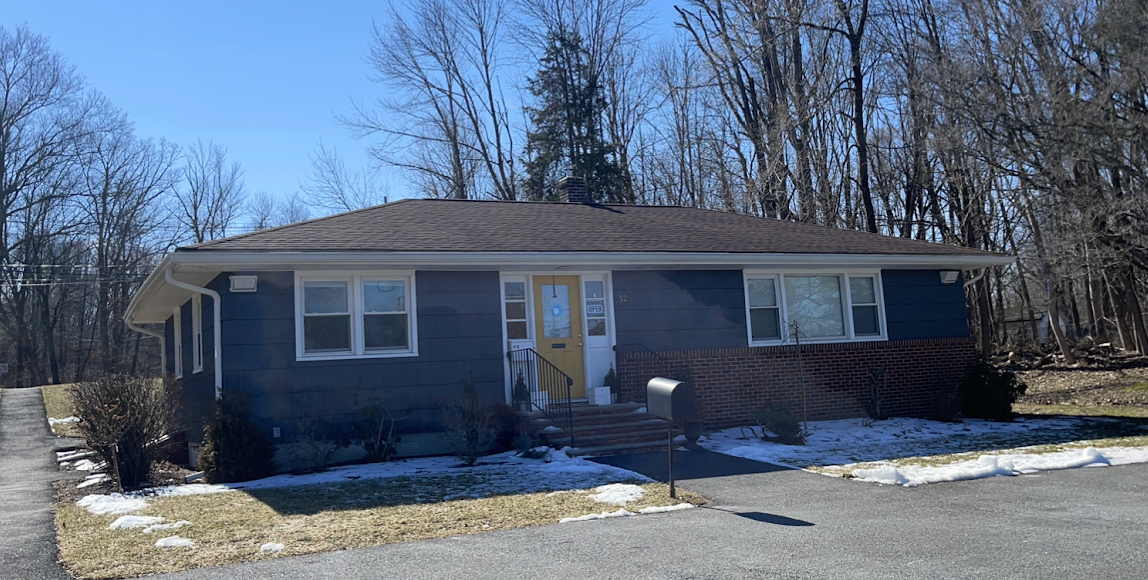 Blue ranch house with white trim and a yellow door, snow on the ground, trees in the background.