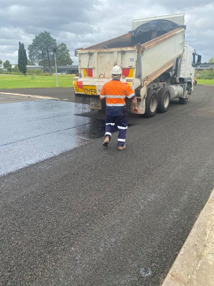 Construction Worker in Safety Vest Watches Asphalt Being Dumped from A Truck — ALI Civil Pty Ltd in Jervis Bay, NSW