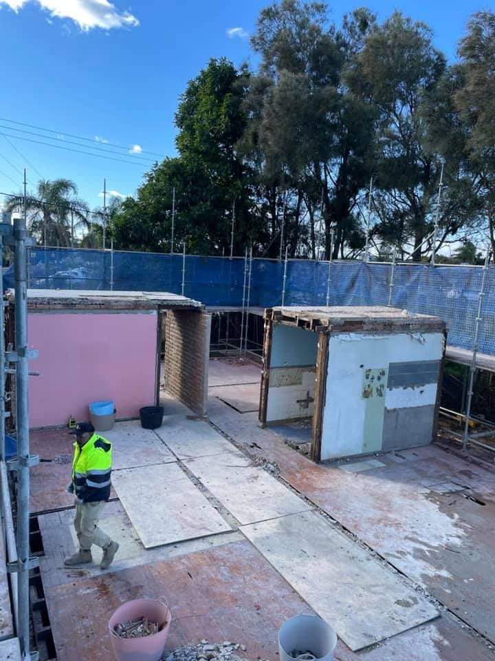 Construction site with two partially demolished structures; worker walks by; blue safety fence. — ALI Civil Pty Ltd in South Nowra, NSW