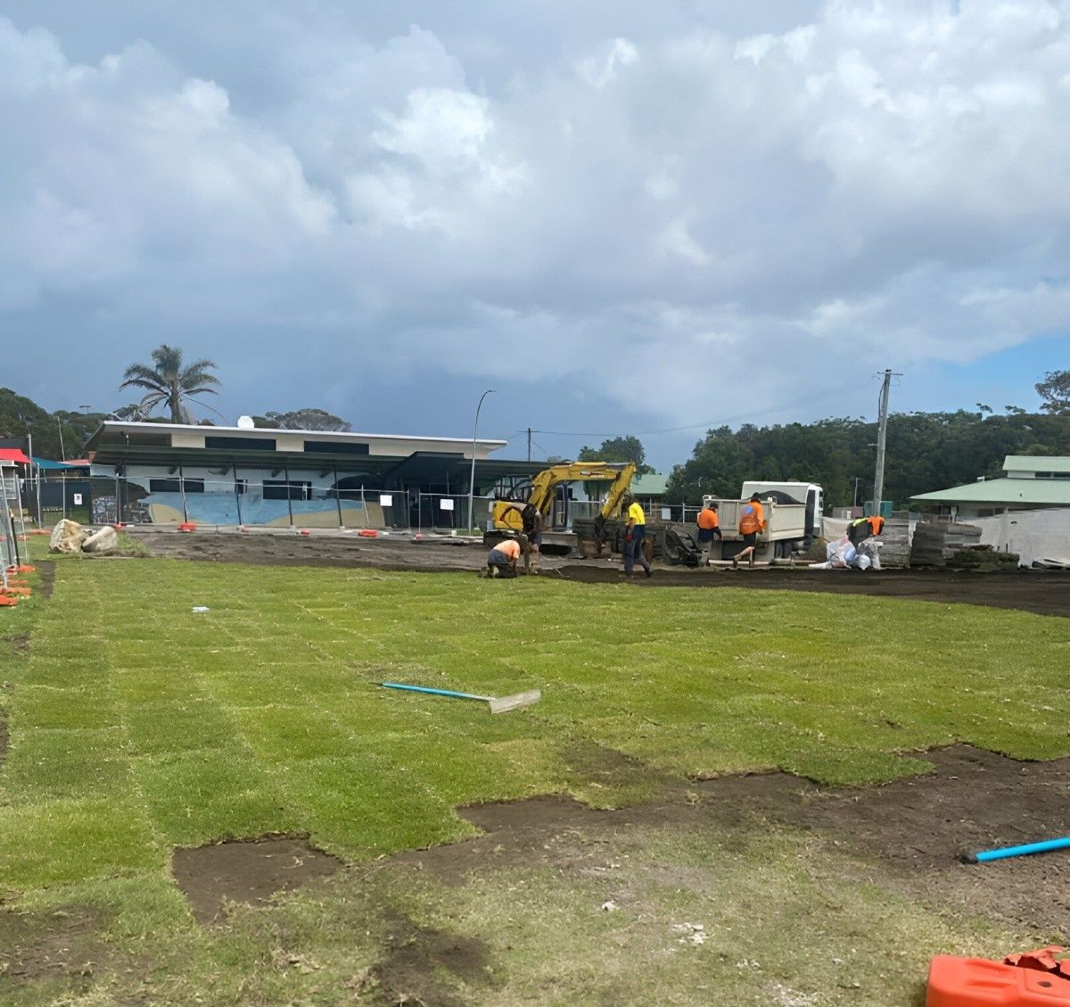 Workers Laying Turf on A Field, with Machinery, and A Building — ALI Civil Pty Ltd in Shellharbour, NSW