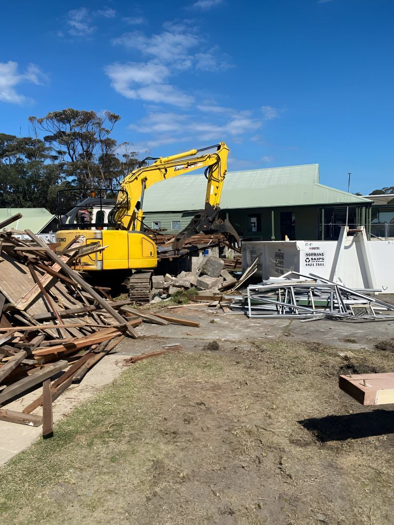 A Yellow Excavator Demolishing a Building on A Sunny Day — ALI Civil Pty Ltd in Jervis Bay, NSW