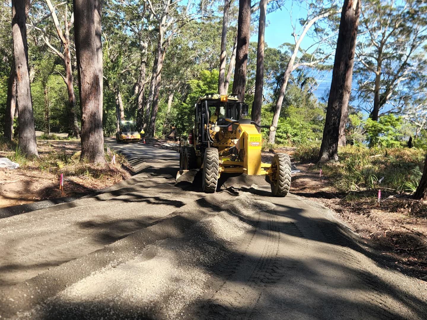 A Yellow Grader Levels a Gravel Road in a Forest — ALI Civil Pty Ltd in Ulladulla, NSW
