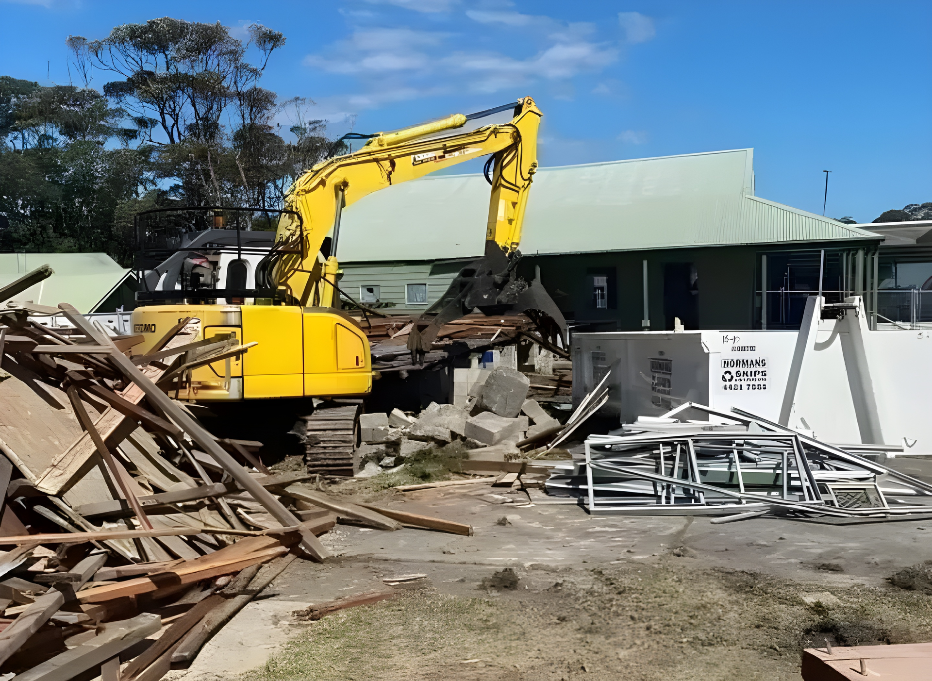 Yellow excavator demolishing a building with a green roof on a sunny day. — ALI Civil Pty Ltd in South Nowra, NSW