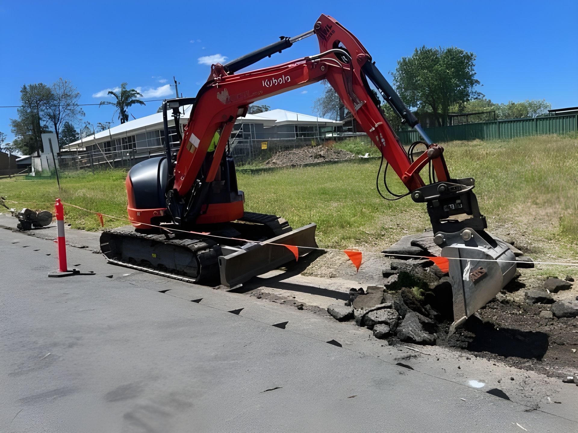 Red Excavator Digging Into Asphalt Curb on a Sunny Day — ALI Civil Pty Ltd in South Nowra, NSW