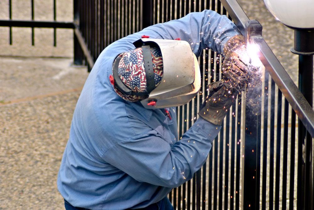 A Man Wearing A Welding Mask Is Welding A Fence — AAA Fencing & Supplies in Southport, QLD