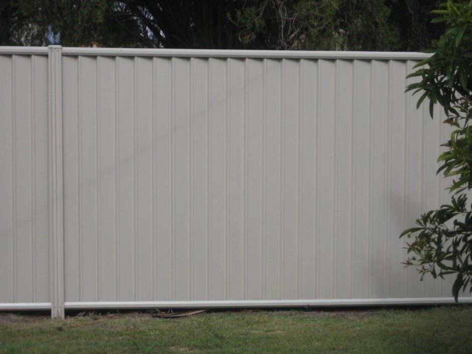 A White Colorbond Fence Is Sitting On Top Of A Lush Green Field — AAA Fencing & Supplies in Southport, QLD