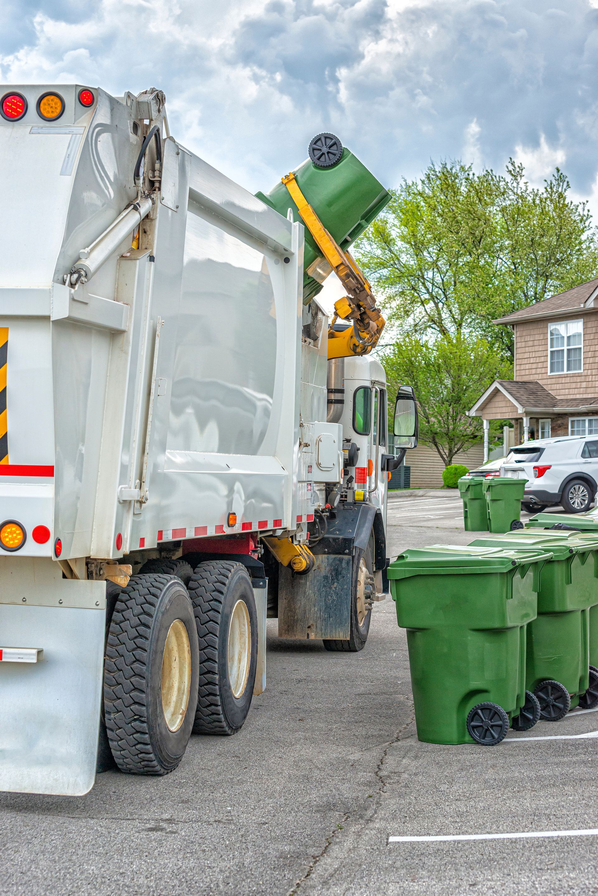 Garbage truck emptying a green bin in a residential area.