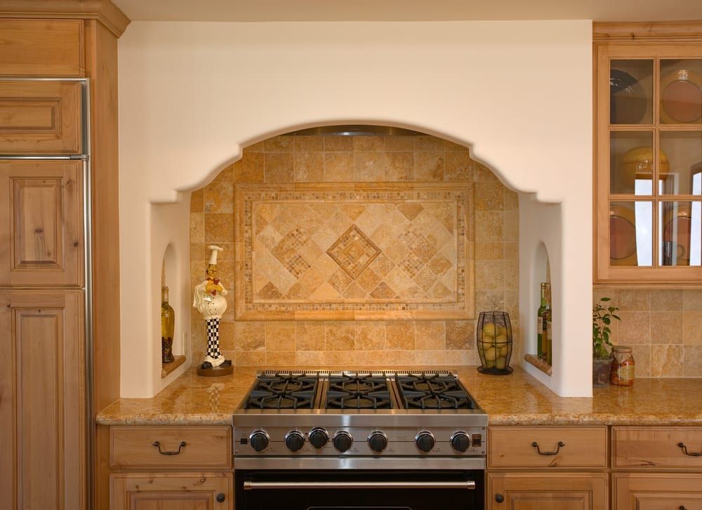 A kitchen stove framed by a tiled, arched alcove with built-in side niches, flanked by wooden cabinets.