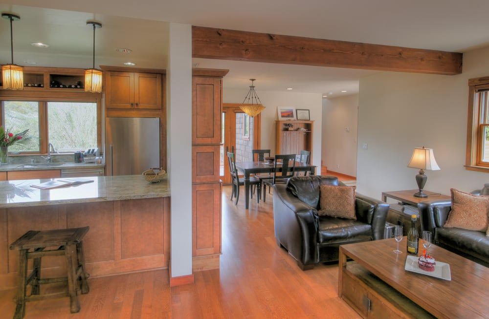 A kitchen with a granite island and stools opens into a living area with dark leather furniture and wood flooring.
