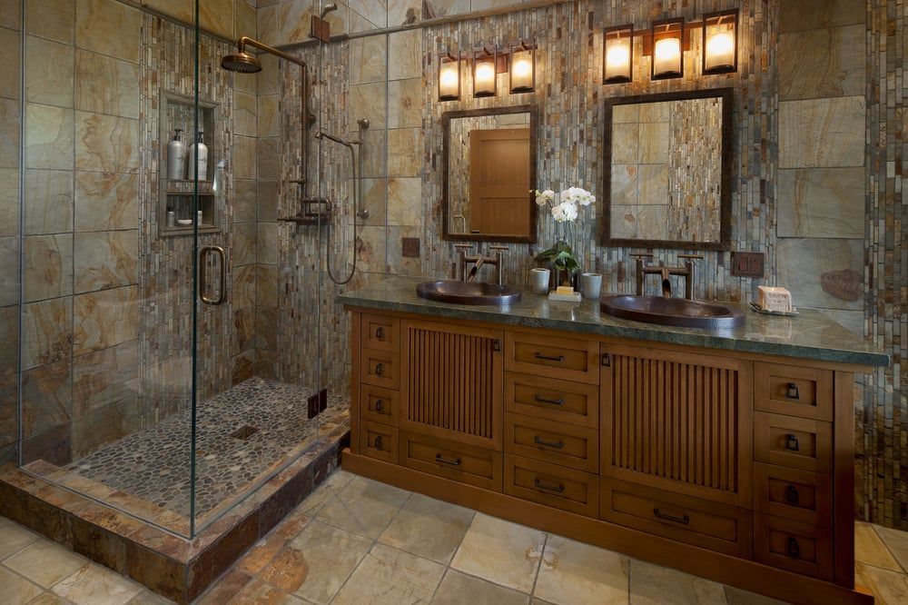 A rustic bathroom featuring a stone walk-in shower with a glass door, a wooden dual-sink vanity, and matching square mirrors.