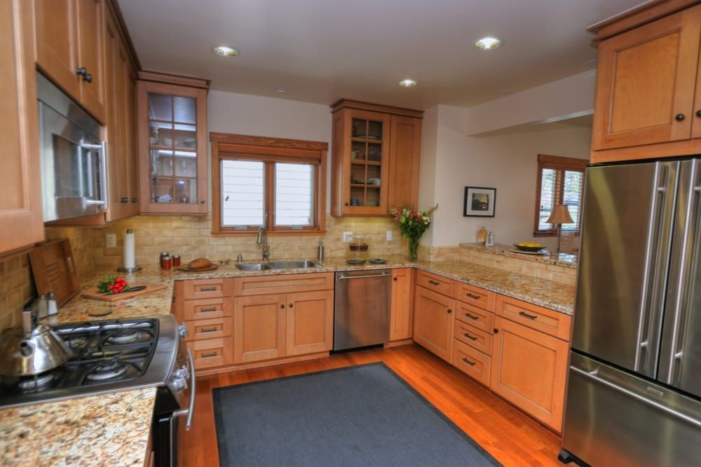 A well-lit kitchen with light wood cabinets, granite countertops, stainless steel appliances, and wood flooring.