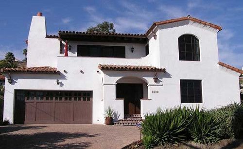 White stucco house with red-tile roof, two-car garage, arched windows, and desert landscaping