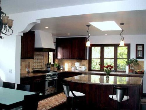 Modern kitchen with dark wood cabinets, black counters, and a large curved island under pendant lights.