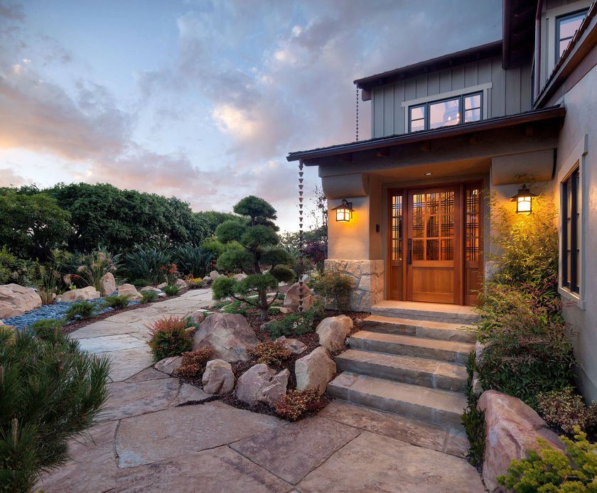 A rustic kitchen features wood cabinets, dark countertops, a center island with bar stools, and hanging copper cookware.