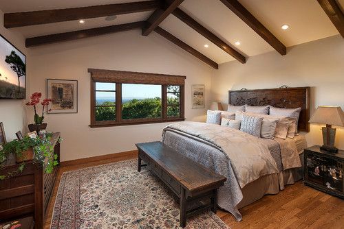 Cozy bedroom with exposed beams, large window, wooden bed, bench, and patterned rug