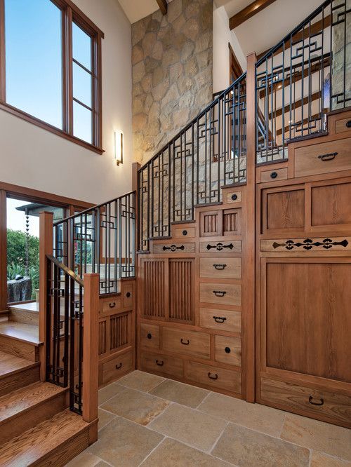 Staircase with ornate wood railing, built-in drawers, and stone tile in a bright home interior